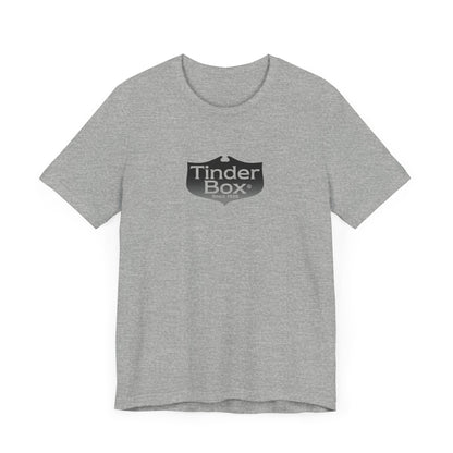 A light blue Printify "The Tinder Box 1980s" unisex jersey short sleeve tee featuring the "Tinder Box" logo in the center. The logo consists of a dark shield with the words "Tinder Box" in white text, with a small flame icon replacing the dot above the "i".