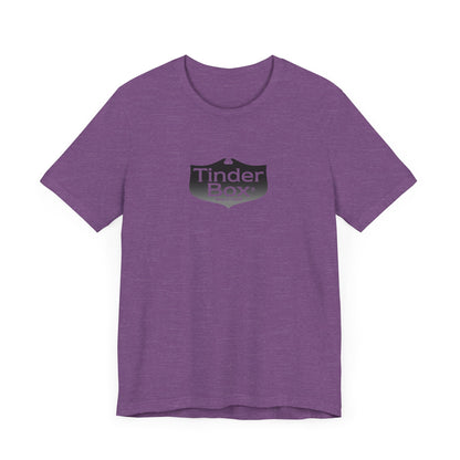 A light blue Printify "The Tinder Box 1980s" unisex jersey short sleeve tee featuring the "Tinder Box" logo in the center. The logo consists of a dark shield with the words "Tinder Box" in white text, with a small flame icon replacing the dot above the "i".