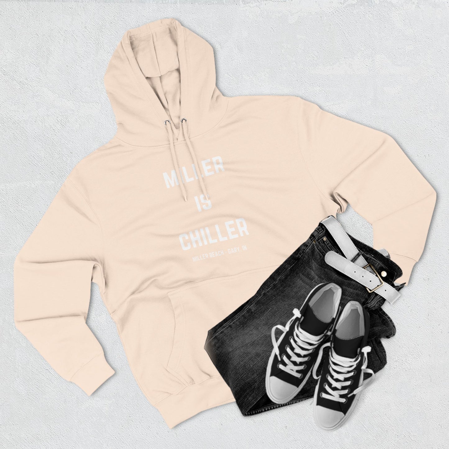 The Miller is Chiller - Miller Beach Three-Panel Fleece Hoodie from Printify features bold white text reading "MILLER IS CHILLER" on the front, with smaller text below stating "MILLER BEACH - GARY, IN." This comfortable black hoodie includes a front pocket and drawstrings.