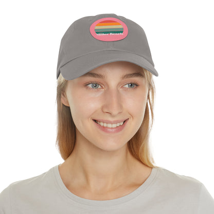 The Miller Beach Retro Sunset - Dad Hat with Leather Patch (Round) by Printify is a pink baseball cap crafted from bio-washed chino twill for added comfort. It features a PU leather patch adorned with horizontal stripes in red, orange, yellow, green, and blue. Below the stripes, "Miller Beach" is embroidered in white. An adjustable strap at the back ensures a perfect fit.