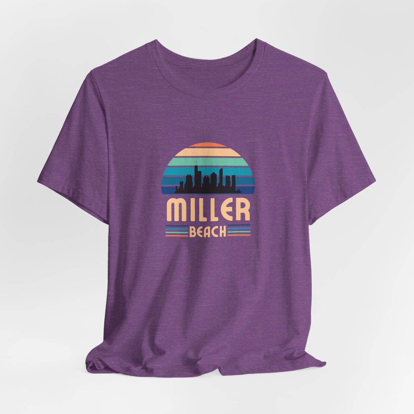 The Printify Miller Beach Chicago Skyline - Unisex Jersey Short Sleeve Tee is a light blue T-shirt featuring a stylized graphic of the Chicago skyline against a setting sun with gradient shades of blue and orange. Below the graphic, "Miller Beach" is printed in bold, yellow letters.