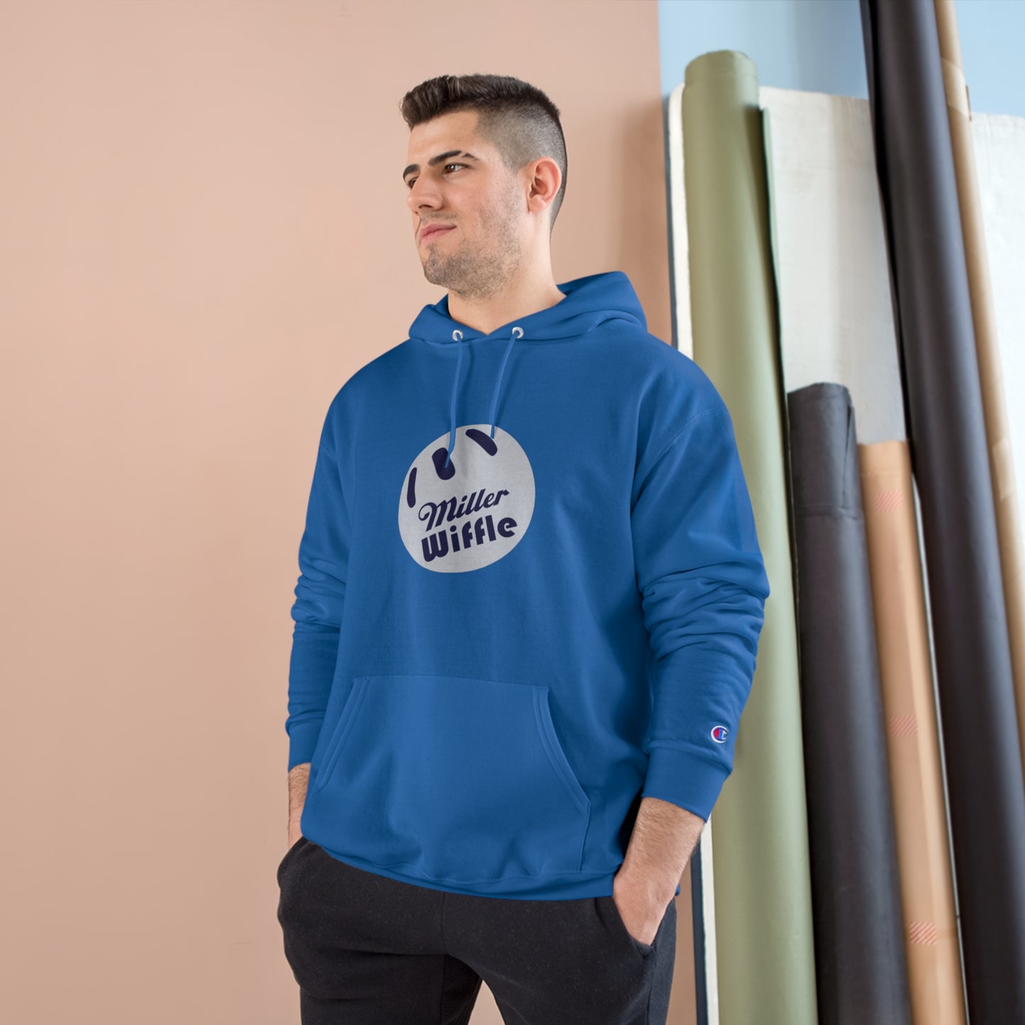 A navy blue Printify Miller Beach Wiffle Ball OG Logo - Sweatshirt, featuring a white wiffle ball graphic on the chest with "Miller Wiffle" in blue beneath it. Made from recycled polyester, this hoodie includes a front pocket, drawstrings, and the Champion logo on the left sleeve. It also offers Double Dry® technology for added comfort.