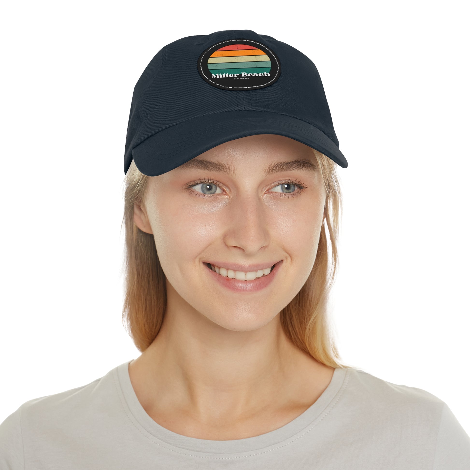 The Miller Beach Retro Sunset - Dad Hat with Leather Patch (Round) by Printify is a pink baseball cap crafted from bio-washed chino twill for added comfort. It features a PU leather patch adorned with horizontal stripes in red, orange, yellow, green, and blue. Below the stripes, "Miller Beach" is embroidered in white. An adjustable strap at the back ensures a perfect fit.