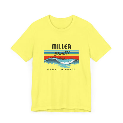 The Miller Beach 46403 Surf Style - Unisex Jersey Short Sleeve Tee by Printify features a retro surf-inspired design on a yellow background. The shirt displays "MILLER BEACH" above waves with a skyline illustration, while "Cary, IN 46403" is printed below the waves. The vibrant design also includes colorful stripes in shades of blue, red, and orange.