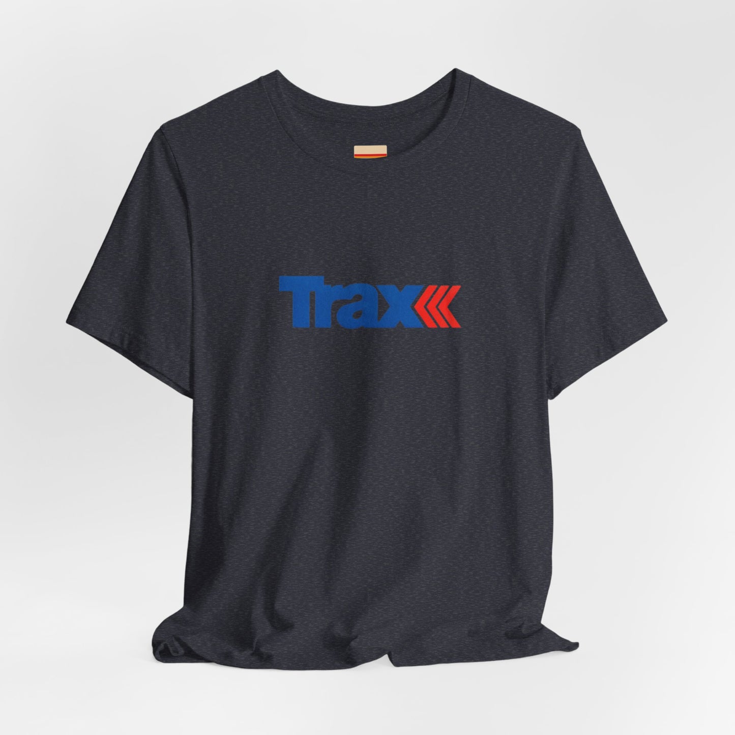 A gray unisex jersey short sleeve tee from Printify, inspired by retro 1980s Kmart style. The "Trax" logo is printed in blue letters, followed by three red arrows pointing to the right. This classic Trax Brand T-shirt is laid flat against a white background, capturing nostalgic fashion vibes.