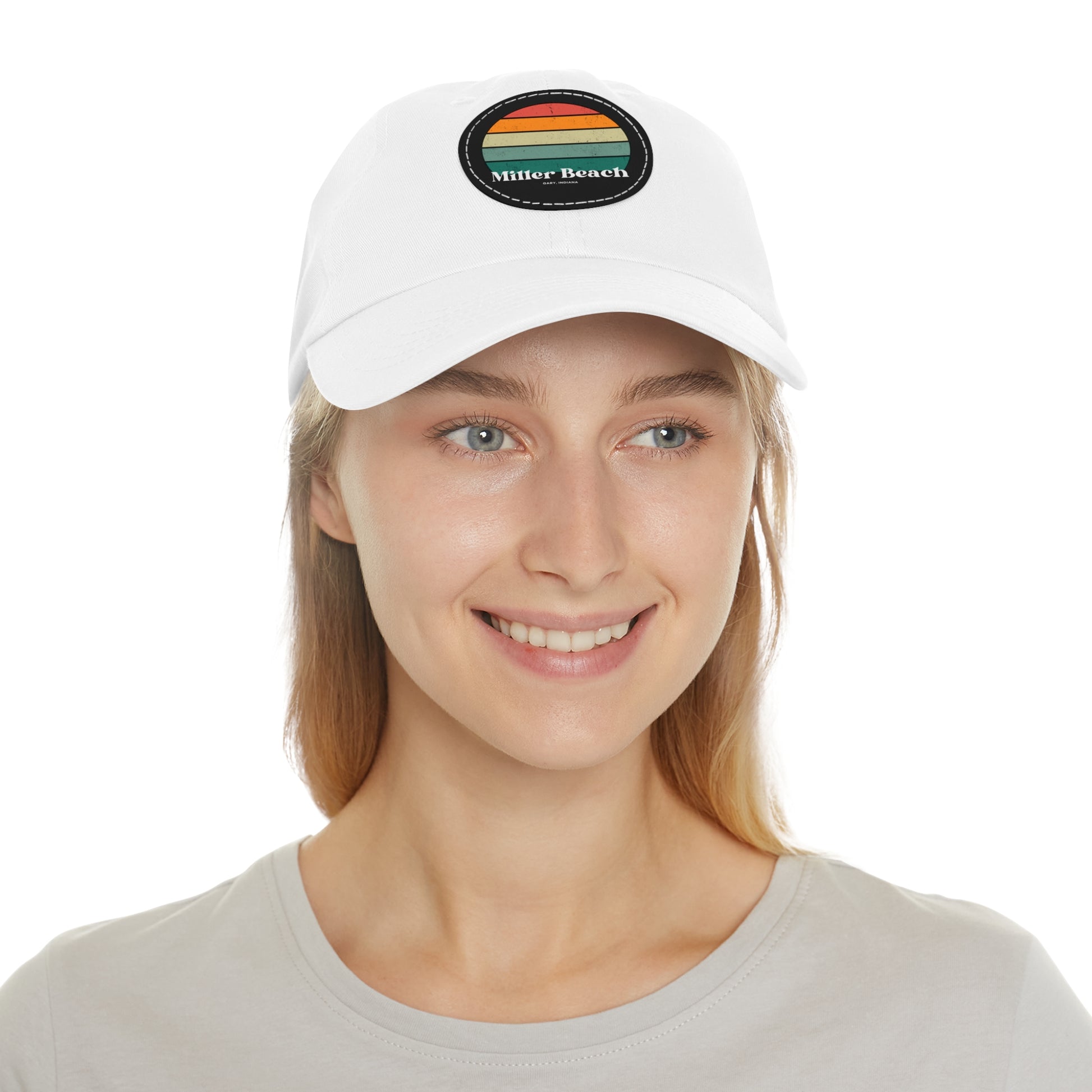 The Miller Beach Retro Sunset - Dad Hat with Leather Patch (Round) by Printify is a pink baseball cap crafted from bio-washed chino twill for added comfort. It features a PU leather patch adorned with horizontal stripes in red, orange, yellow, green, and blue. Below the stripes, "Miller Beach" is embroidered in white. An adjustable strap at the back ensures a perfect fit.