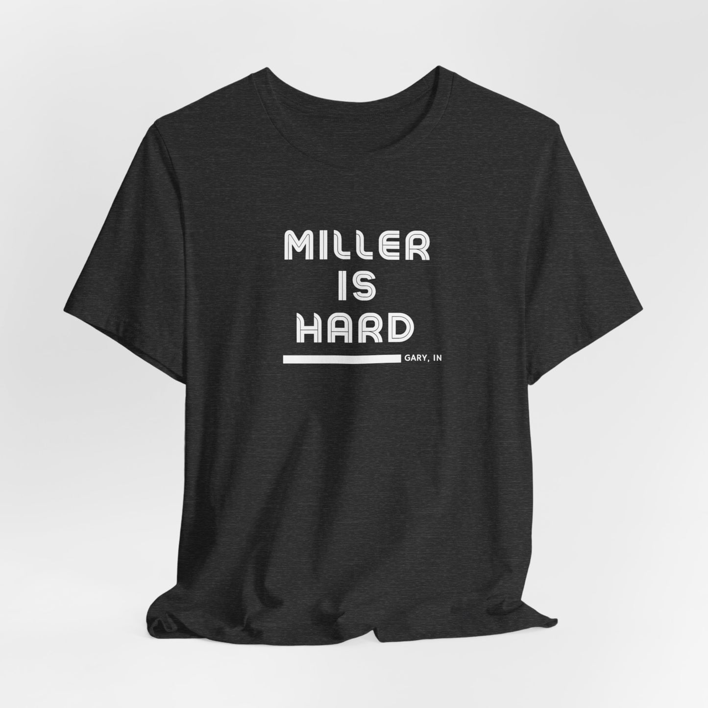 The Miller is Hard - White Letters - Unisex Jersey Short Sleeve Tee by Printify features a rust-colored design with "MILLER IS HARD" printed in bold, white capitals on the front. Below, "GARY, IN." is added in smaller font. This simple yet striking shirt evokes the spirit of Miller Beach with no additional graphics or patterns.