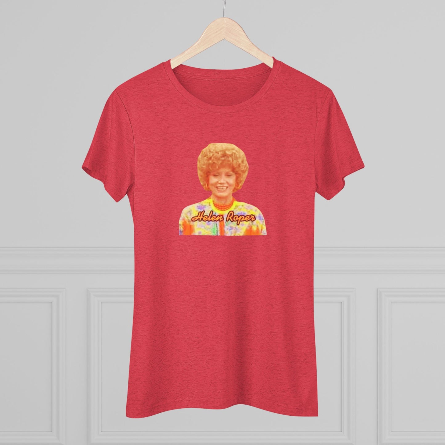 A Women's Triblend Tee by Printify, titled "Helen Roper - Three's Company," features a red design with an illustration of a smiling person with curly hair and colorful clothing. Below the illustration, the text "Helen Roper" is written in a bold, retro font, capturing the essence of vintage TV humor.