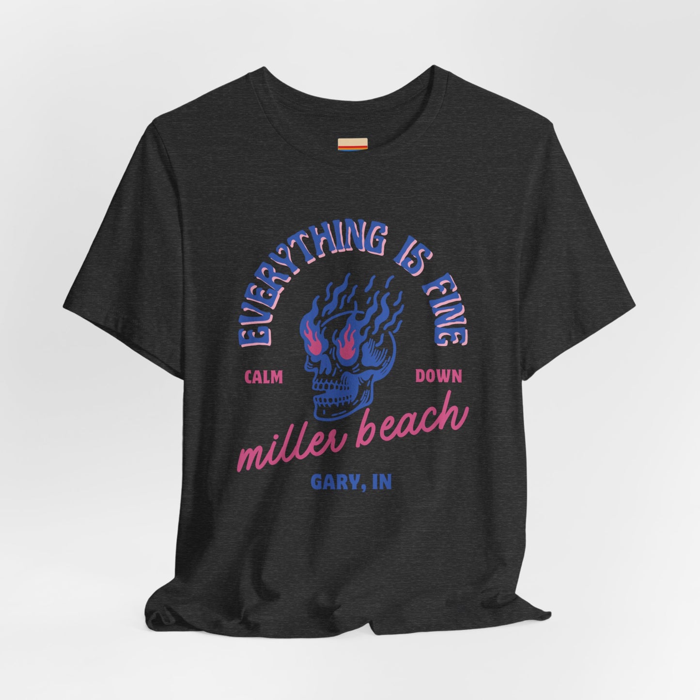 The Miller Beach Calm Down Everything is Fine - Unisex Jersey Short Sleeve Tee from Printify, crafted from soft Airlume combed cotton, showcases a peach-colored design with a flaming skull in the center. Above the design, it reads "Everything is fine," and below it says, "Calm down Miller Beach." In smaller text at the bottom, it reads "Gary, IN.