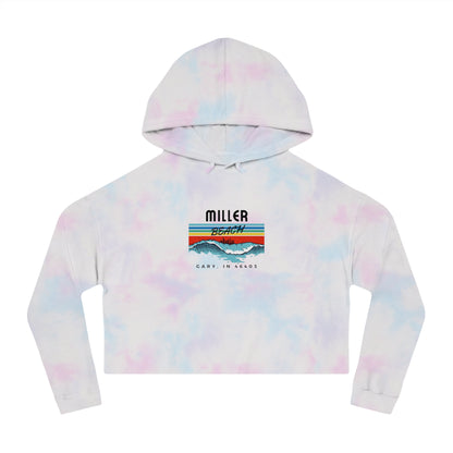 Introducing the Miller Beach Surf Women's Cropped Hooded Sweatshirt by Printify, a white personalized hoodie featuring a pastel tie-dye pattern. The front showcases a bold "Miller Beach" graphic above "Gary, IN" on a vibrant striped background with stylized mountains and waves. This long-sleeve hoodie comes in a trendy cropped style complete with a drawstring hood.