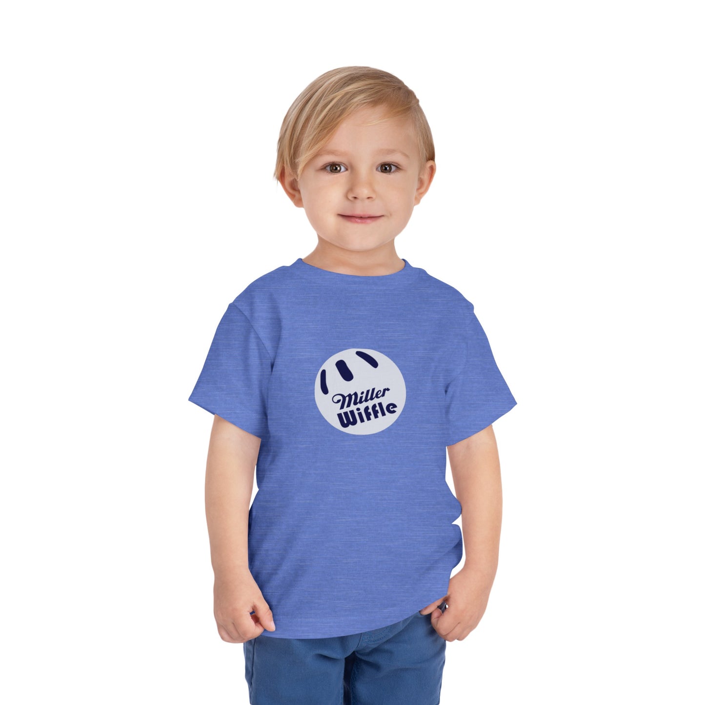 A young child with light hair stands against a plain white background, smiling while wearing a vibrant yellow Printify short sleeve tee named "Miller Wiffel Ball OG Logo - Toddler Short Sleeve Tee." The shirt features the "Miller Wiffle" text and a wiffle ball graphic on the front. The child is also dressed in blue pants.