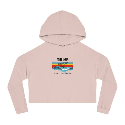 Introducing the Miller Beach Surf Women's Cropped Hooded Sweatshirt by Printify, a white personalized hoodie featuring a pastel tie-dye pattern. The front showcases a bold "Miller Beach" graphic above "Gary, IN" on a vibrant striped background with stylized mountains and waves. This long-sleeve hoodie comes in a trendy cropped style complete with a drawstring hood.