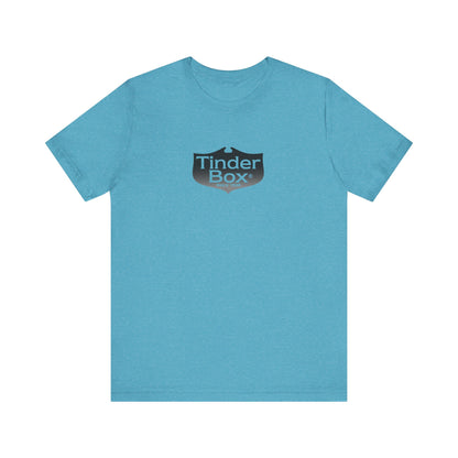 A light blue Printify "The Tinder Box 1980s" unisex jersey short sleeve tee featuring the "Tinder Box" logo in the center. The logo consists of a dark shield with the words "Tinder Box" in white text, with a small flame icon replacing the dot above the "i".