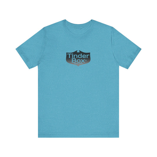 A light blue Printify "The Tinder Box 1980s" unisex jersey short sleeve tee featuring the "Tinder Box" logo in the center. The logo consists of a dark shield with the words "Tinder Box" in white text, with a small flame icon replacing the dot above the "i".