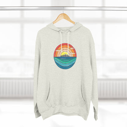 The Miller Beach Abstract - Three-Panel Fleece Hoodie by Printify is a premium light gray pullover featuring a vibrant circular front design. It showcases an abstract sunset-over-ocean scene with blue waters, an orange to red gradient sky, and a city skyline silhouette. Made from soft combed ring-spun cotton and lined with cozy fleece for extra warmth.