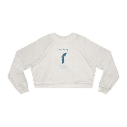 The "Just the Tip - Miller Beach" Women's Cropped Fleece Pullover by Printify is a beige sweatshirt with long sleeves and a crew neck. It features a blue-green abstract feather design in the center with the words "Just the tip" above it, and "Silly Peach" along with "Gary, IN." below. This pullover is crafted from premium tri-blend fabric for ultimate comfort and style.