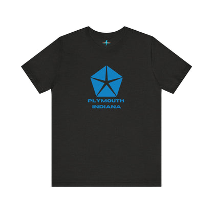 A black Printify Plymouth, Indiana Chrysler Logo T-shirt is displayed against a plain white background. The shirt features a blue, five-point star emblem reminiscent of a vintage autos design above the text "PLYMOUTH INDIANA" in blue, centered across the front. The shirt is laid out flat with the sleeves slightly bent.