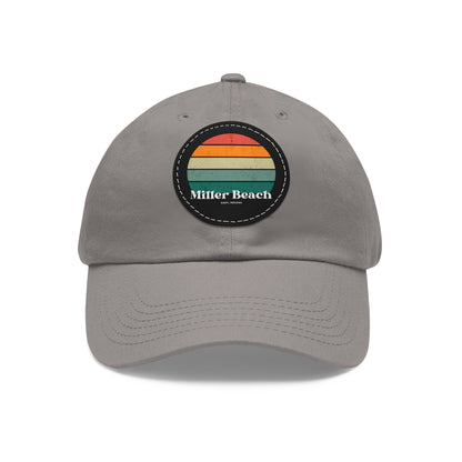 The Miller Beach Retro Sunset - Dad Hat with Leather Patch (Round) by Printify is a pink baseball cap crafted from bio-washed chino twill for added comfort. It features a PU leather patch adorned with horizontal stripes in red, orange, yellow, green, and blue. Below the stripes, "Miller Beach" is embroidered in white. An adjustable strap at the back ensures a perfect fit.