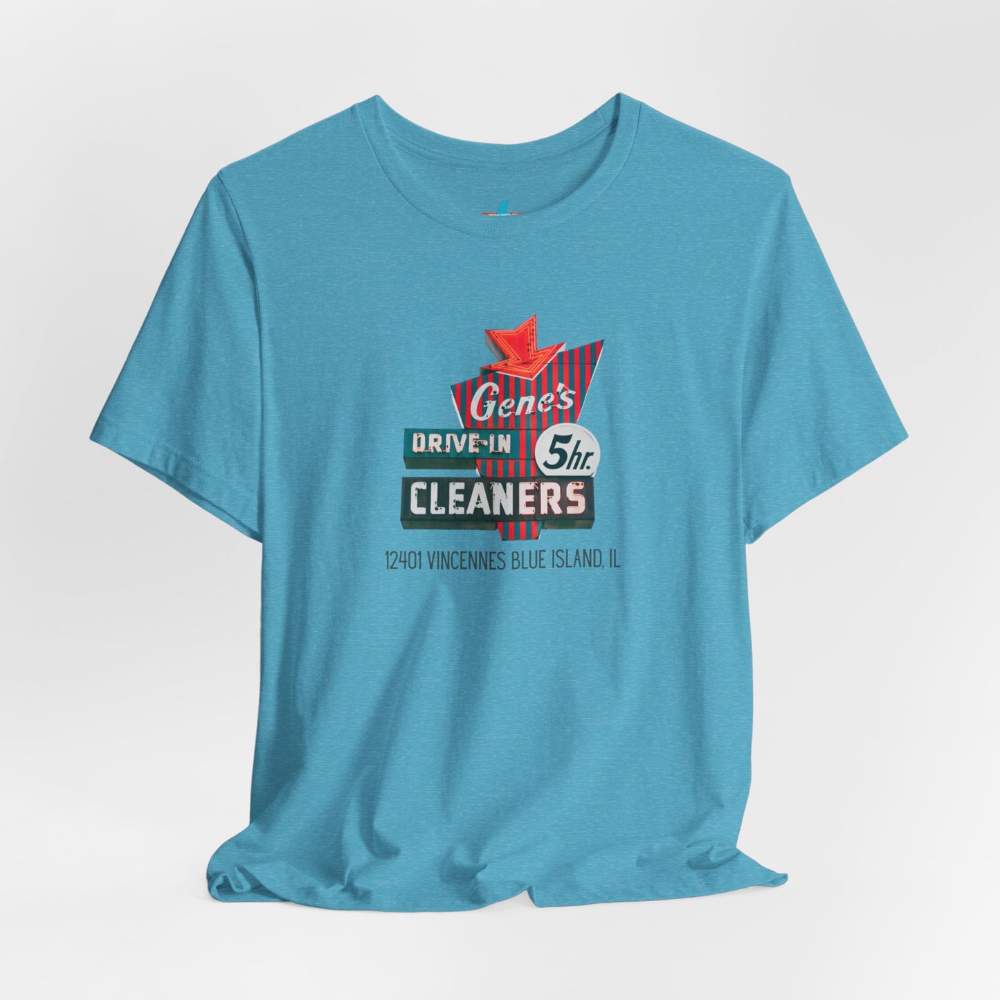 A unisex Jersey short sleeve tee from Printify featuring a light grey color with a retro-style graphic in the center. The design showcases text that reads "Gene's Drive In Cleaners, 5th," along with the address "12401 Vincennes Blue Island IL" in a blend of vintage fonts and colors, evoking the classic Chicago Fire-era vintage sign aesthetic.