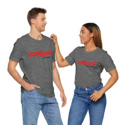 A smiling man and woman interact while wearing matching yellow "Hot Dog The Movie 1984 - Unisex Jersey Short Sleeve Tee" by Printify, featuring bold red "HOT DOG THE MOVIE" text. Their vibrant tees perfectly complement their blue jeans, with the man casually having his hands in his pockets and the woman resting one hand on his shoulder.