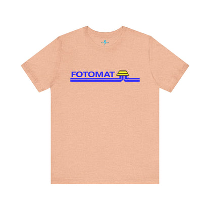 The Fotomat 1970s Retro T-Shirt by Printify is a dark gray short-sleeve shirt that features the word "FOTOMAT" in bold blue capital letters and a blue and yellow graphic design resembling layered lines and an upside-down triangle. This Tshirt captures the essence of 80s nostalgia with its centered, retro design.