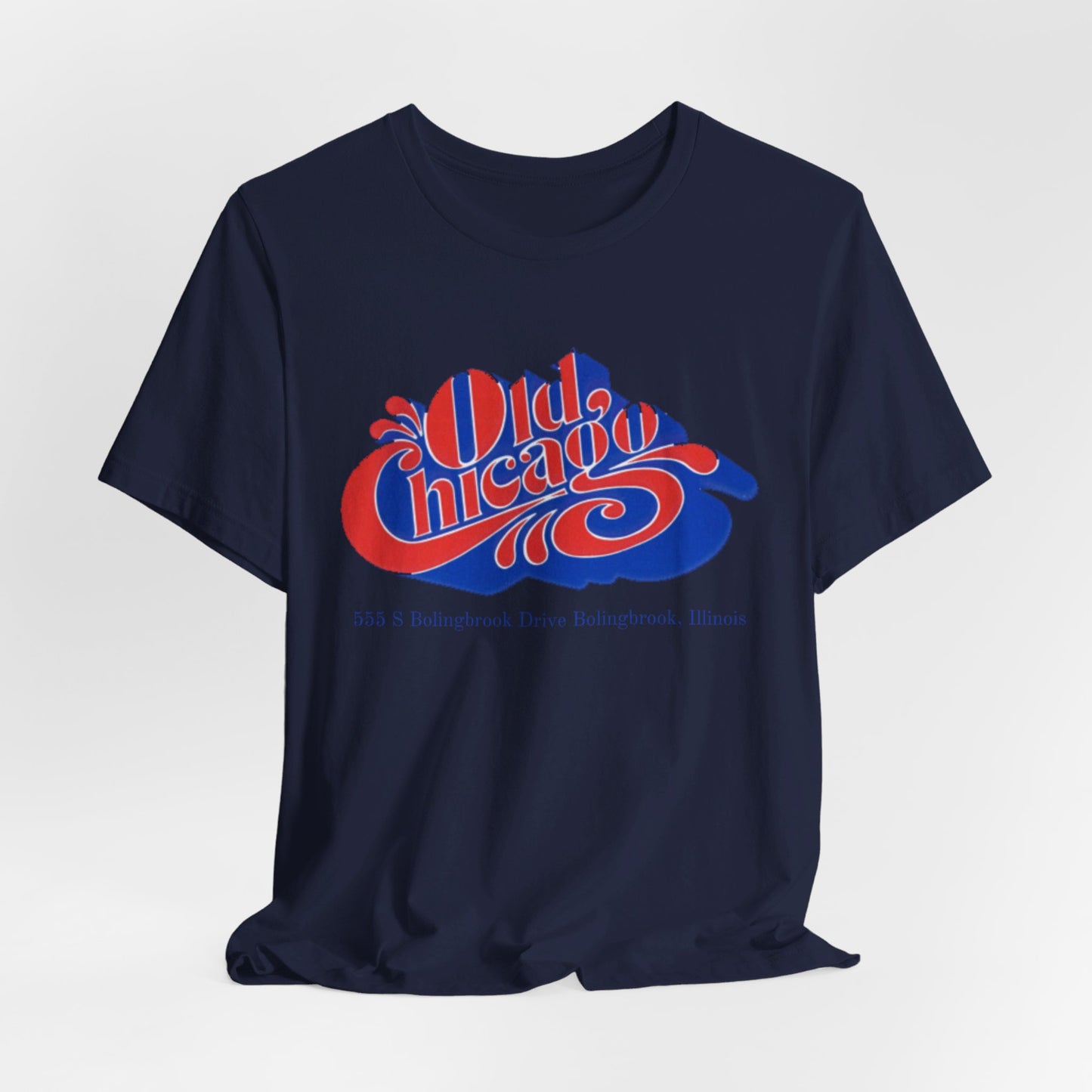 The "Old Chicago Mall Bolingbrook 1980s Retro - Unisex Jersey Short Sleeve Tee" from Printify is a gray T-shirt showcasing a vintage design with the text "Old Chicago" in blue and red. Beneath the main text, the address "355 S. Bolingbrook Drive, Bolingbrook, Illinois" appears in smaller font, evoking 80s nostalgia of the Old Chicago Mall. The shirt is displayed against a white background.