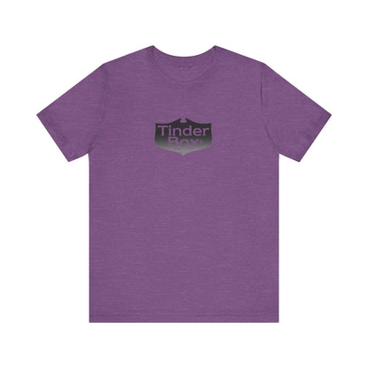 A light blue Printify "The Tinder Box 1980s" unisex jersey short sleeve tee featuring the "Tinder Box" logo in the center. The logo consists of a dark shield with the words "Tinder Box" in white text, with a small flame icon replacing the dot above the "i".