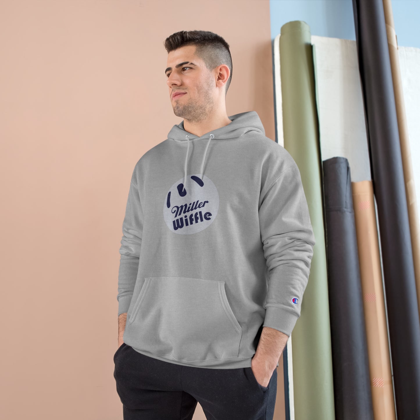 A navy blue Printify Miller Beach Wiffle Ball OG Logo - Sweatshirt, featuring a white wiffle ball graphic on the chest with "Miller Wiffle" in blue beneath it. Made from recycled polyester, this hoodie includes a front pocket, drawstrings, and the Champion logo on the left sleeve. It also offers Double Dry® technology for added comfort.