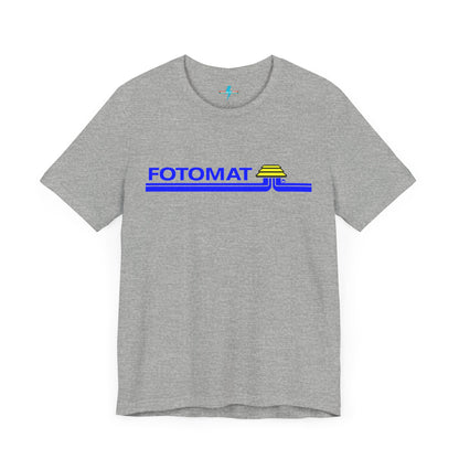 The Fotomat 1970s Retro T-Shirt by Printify is a dark gray short-sleeve shirt that features the word "FOTOMAT" in bold blue capital letters and a blue and yellow graphic design resembling layered lines and an upside-down triangle. This Tshirt captures the essence of 80s nostalgia with its centered, retro design.