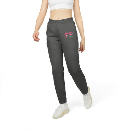 A person is confidently dressed in the cozy Miller Beach Flamingos - Adidas Unisex Fleece Joggers from Printify, featuring "Myrtle Beach" and "Yearround" text in pink and green on the left thigh. They complete their look with a white shirt and gray sneakers, standing against a plain white background.