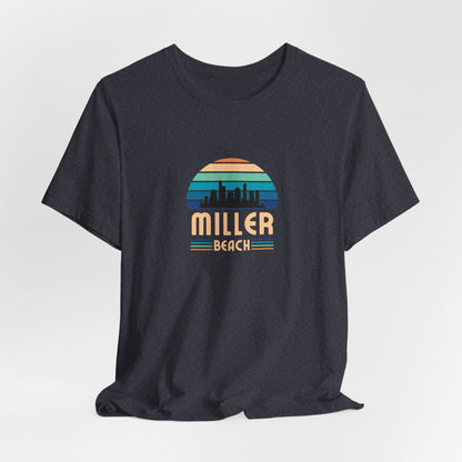 A brown unisex jersey short sleeve tee called "Miller Beach Chicago Skyline" from Printify features a vintage-style design with a sunset, the Chicago skyline, and "Miller Beach" in bold letters. The design incorporates shades of blue, orange, and yellow and is displayed against a plain white background.