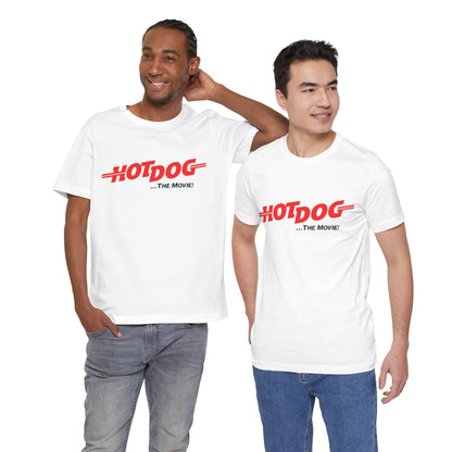 A smiling man and woman interact while wearing matching yellow "Hot Dog The Movie 1984 - Unisex Jersey Short Sleeve Tee" by Printify, featuring bold red "HOT DOG THE MOVIE" text. Their vibrant tees perfectly complement their blue jeans, with the man casually having his hands in his pockets and the woman resting one hand on his shoulder.