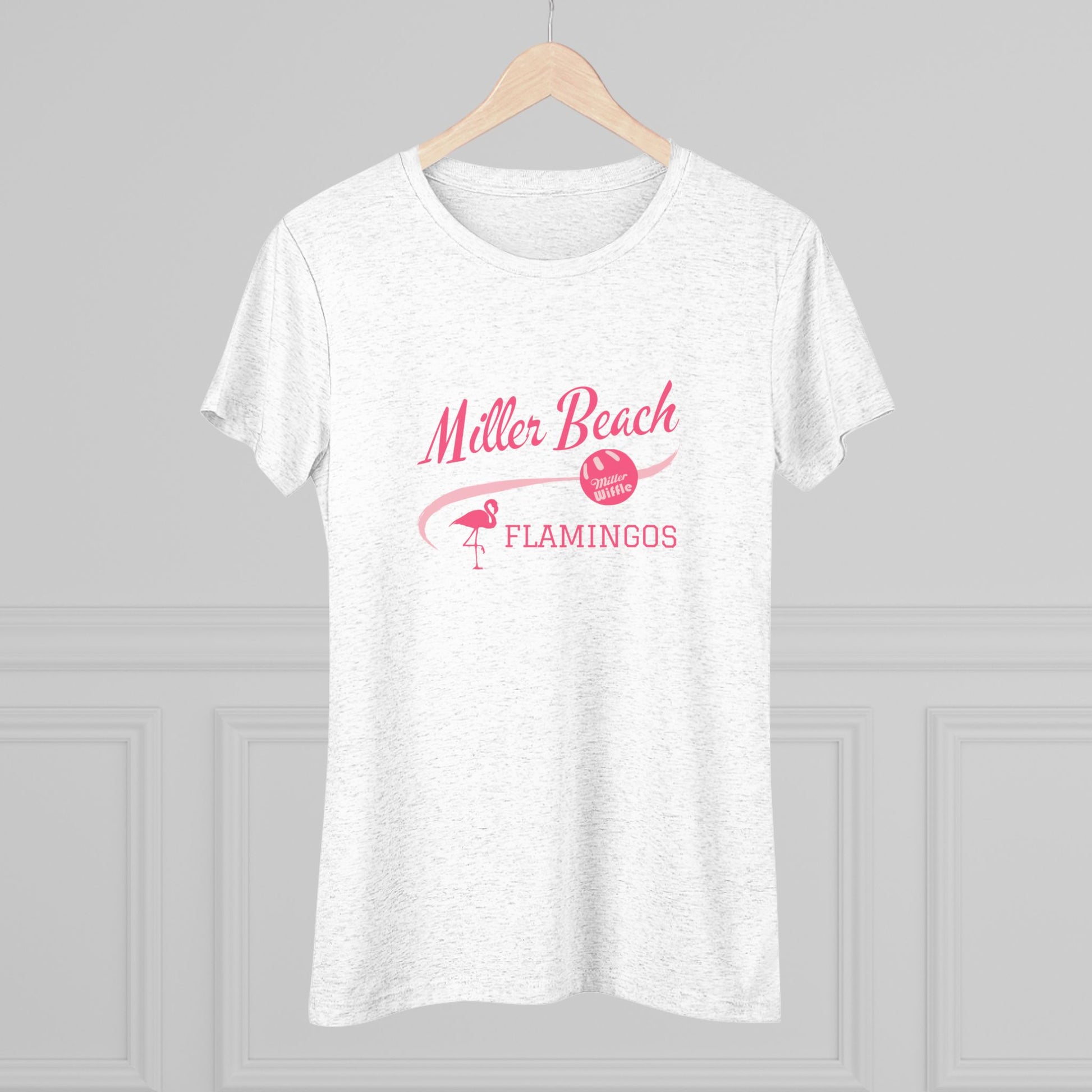 The Printify Miller Beach Wiffel Ball - Flamingos Women's Triblend Tee is a dark gray shirt featuring the text "Miller Beach Flamingos" in pink. The design showcases a flamingo standing on one foot beside a beach volleyball, exuding a fun and relaxed beach atmosphere. This limited edition tee is ideal for celebrating the World Championship of Wiff Ball.