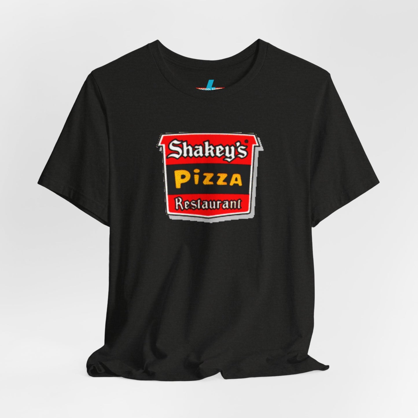 A black Shakey's Pizza - 1980s Retro Logo - Unisex T-Shirt by Printify hangs against a white background. The shirt features a colorful graphic with the text "Shakey's Pizza Restaurant" in white, yellow, and black lettering on a red background, resembling vintage pizza joints signage. This retro tee brings nostalgic vibes of classic pizzerias.