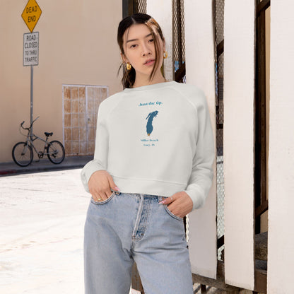 The "Just the Tip - Miller Beach" Women's Cropped Fleece Pullover by Printify is a beige sweatshirt with long sleeves and a crew neck. It features a blue-green abstract feather design in the center with the words "Just the tip" above it, and "Silly Peach" along with "Gary, IN." below. This pullover is crafted from premium tri-blend fabric for ultimate comfort and style.