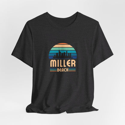 The Printify Miller Beach Chicago Skyline - Unisex Jersey Short Sleeve Tee is a light blue T-shirt featuring a stylized graphic of the Chicago skyline against a setting sun with gradient shades of blue and orange. Below the graphic, "Miller Beach" is printed in bold, yellow letters.