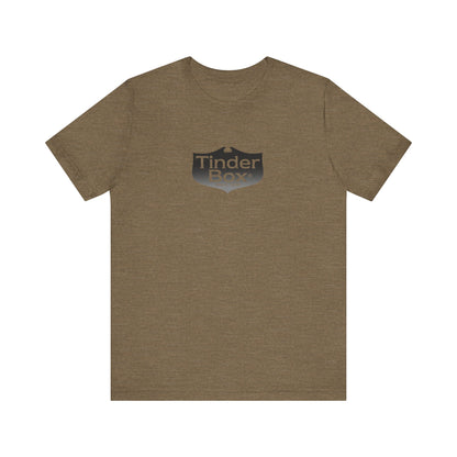 A light blue Printify "The Tinder Box 1980s" unisex jersey short sleeve tee featuring the "Tinder Box" logo in the center. The logo consists of a dark shield with the words "Tinder Box" in white text, with a small flame icon replacing the dot above the "i".