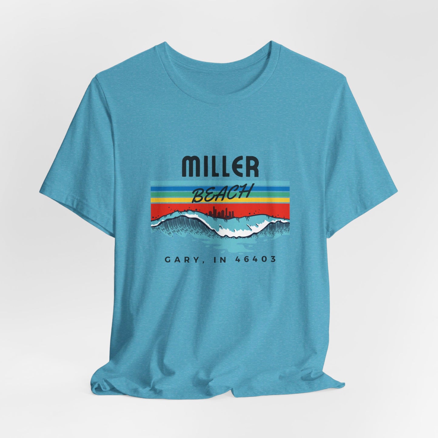 The Miller Beach 46403 Surf Style - Unisex Jersey Short Sleeve Tee by Printify features a retro surf-inspired design on a yellow background. The shirt displays "MILLER BEACH" above waves with a skyline illustration, while "Cary, IN 46403" is printed below the waves. The vibrant design also includes colorful stripes in shades of blue, red, and orange.