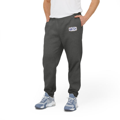 These gray fleece joggers by Printify, named "Blues Brothers License Plate - BDR529 - Adidas Fleece Joggers," feature an iconic Adidas logo on the left thigh and a patch with "BDR529" on the right thigh, evoking retro movie nostalgia. Designed with an elastic waistband and cuffs, these joggers offer both style and comfort.