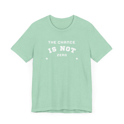 Folded light red Unisex Jersey Short Sleeve Tee from Printify, featuring bold white text that reads "THE CHANCE IS NOT ZERO" along with two star illustrations. This motivational T-shirt, made from breathable fabric, is neatly stacked with another identical shirt underneath.