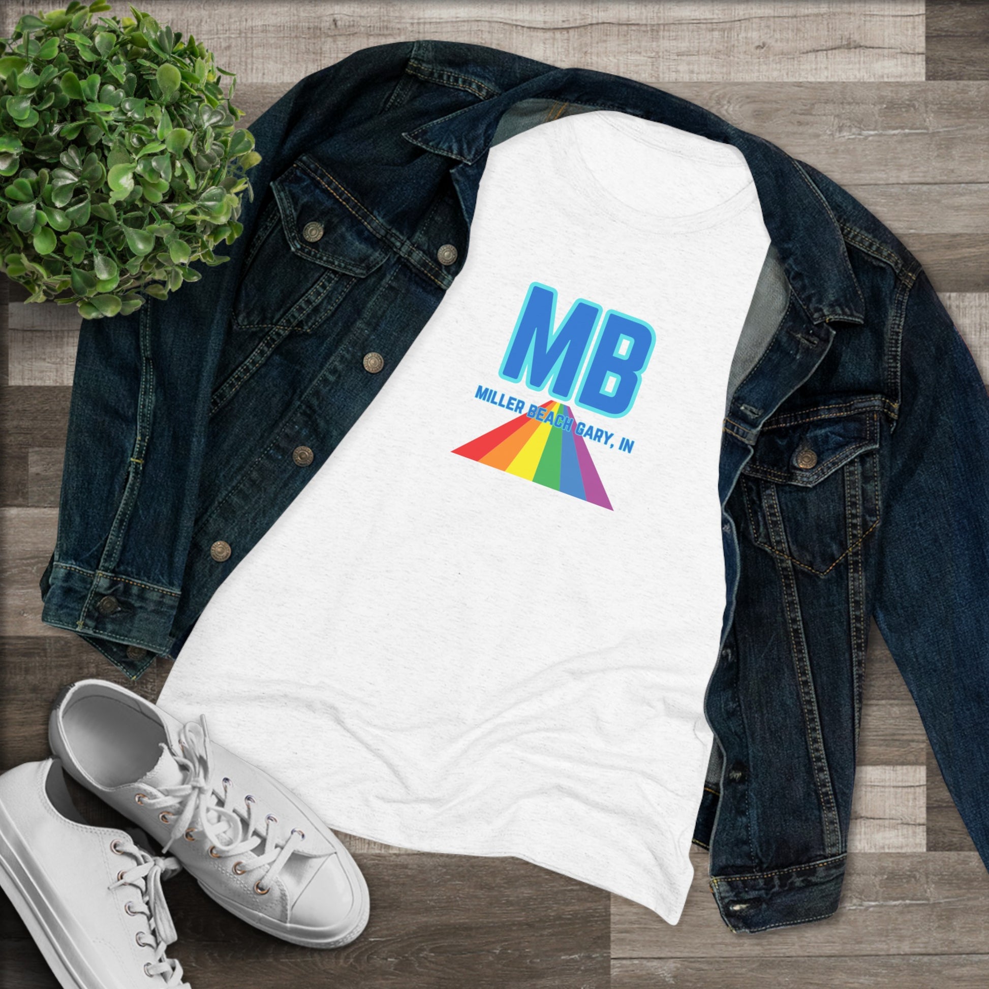 The Miller Beach Pride - Women's Triblend Tee by Printify is a dark gray, cozy t-shirt with a vintage look, featuring the text "MB" in large blue letters at the center. Below the letters, there is a rainbow-colored triangular design with "Millions & Binary, Inc." written in smaller text under the rainbow triangle.