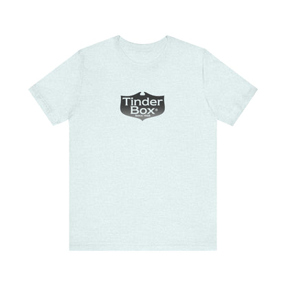 A light blue Printify "The Tinder Box 1980s" unisex jersey short sleeve tee featuring the "Tinder Box" logo in the center. The logo consists of a dark shield with the words "Tinder Box" in white text, with a small flame icon replacing the dot above the "i".