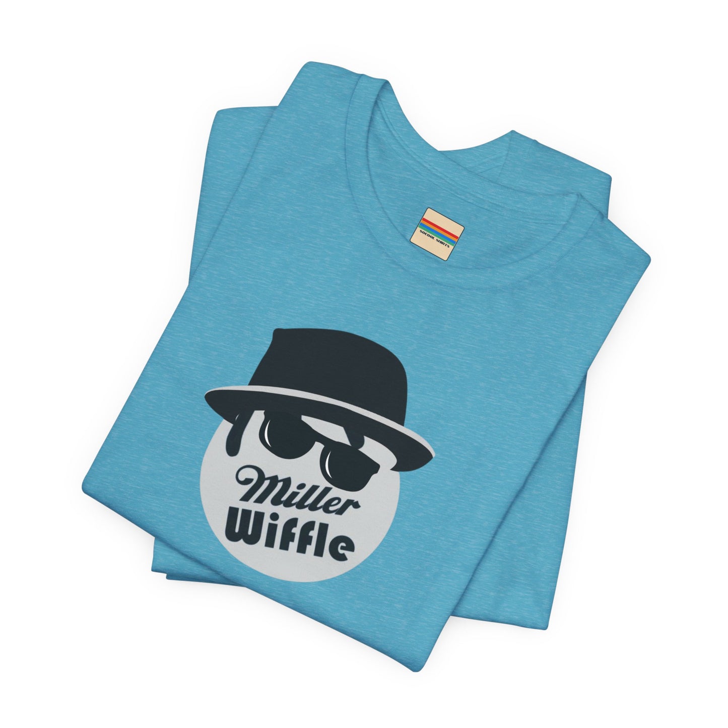 A purple unisex jersey tee from Printify, named the "Miller Wiffel Ball - Blues Brothers - Unisex Jersey Short Sleeve Tee," features a stylized graphic of a ball wearing a black fedora and sunglasses with the text "Miller Wiffel" below it. Another identical soft cotton t-shirt is neatly folded underneath, highlighting its breathable fabric.