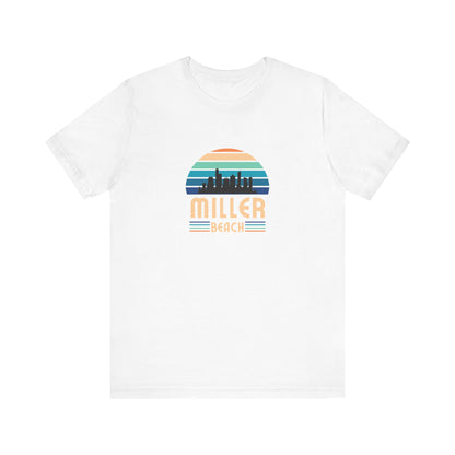 The Printify Miller Beach Chicago Skyline - Unisex Jersey Short Sleeve Tee is a light blue T-shirt featuring a stylized graphic of the Chicago skyline against a setting sun with gradient shades of blue and orange. Below the graphic, "Miller Beach" is printed in bold, yellow letters.