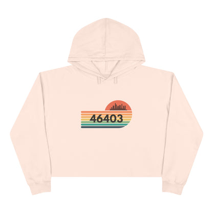 The Miller Beach 46403 Women's Crop Hoodie by Printify features a nostalgic design with a city skyline silhouette and the iconic "46403" zip code, set against a striped sunset backdrop in vibrant orange, green, and yellow hues that capture the essence of Miller Beach.