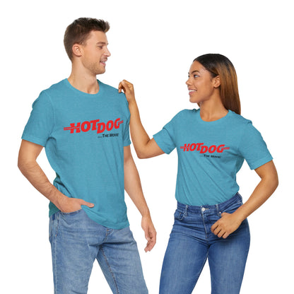 A smiling man and woman interact while wearing matching yellow "Hot Dog The Movie 1984 - Unisex Jersey Short Sleeve Tee" by Printify, featuring bold red "HOT DOG THE MOVIE" text. Their vibrant tees perfectly complement their blue jeans, with the man casually having his hands in his pockets and the woman resting one hand on his shoulder.