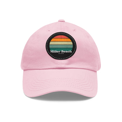 The Miller Beach Retro Sunset - Dad Hat with Leather Patch (Round) by Printify is a pink baseball cap crafted from bio-washed chino twill for added comfort. It features a PU leather patch adorned with horizontal stripes in red, orange, yellow, green, and blue. Below the stripes, "Miller Beach" is embroidered in white. An adjustable strap at the back ensures a perfect fit.