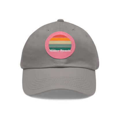 The Miller Beach Retro Sunset - Dad Hat with Leather Patch (Round) by Printify is a pink baseball cap crafted from bio-washed chino twill for added comfort. It features a PU leather patch adorned with horizontal stripes in red, orange, yellow, green, and blue. Below the stripes, "Miller Beach" is embroidered in white. An adjustable strap at the back ensures a perfect fit.