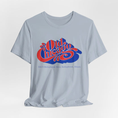 The "Old Chicago Mall Bolingbrook 1980s Retro - Unisex Jersey Short Sleeve Tee" from Printify is a gray T-shirt showcasing a vintage design with the text "Old Chicago" in blue and red. Beneath the main text, the address "355 S. Bolingbrook Drive, Bolingbrook, Illinois" appears in smaller font, evoking 80s nostalgia of the Old Chicago Mall. The shirt is displayed against a white background.