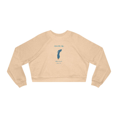 The "Just the Tip - Miller Beach" Women's Cropped Fleece Pullover by Printify is a beige sweatshirt with long sleeves and a crew neck. It features a blue-green abstract feather design in the center with the words "Just the tip" above it, and "Silly Peach" along with "Gary, IN." below. This pullover is crafted from premium tri-blend fabric for ultimate comfort and style.